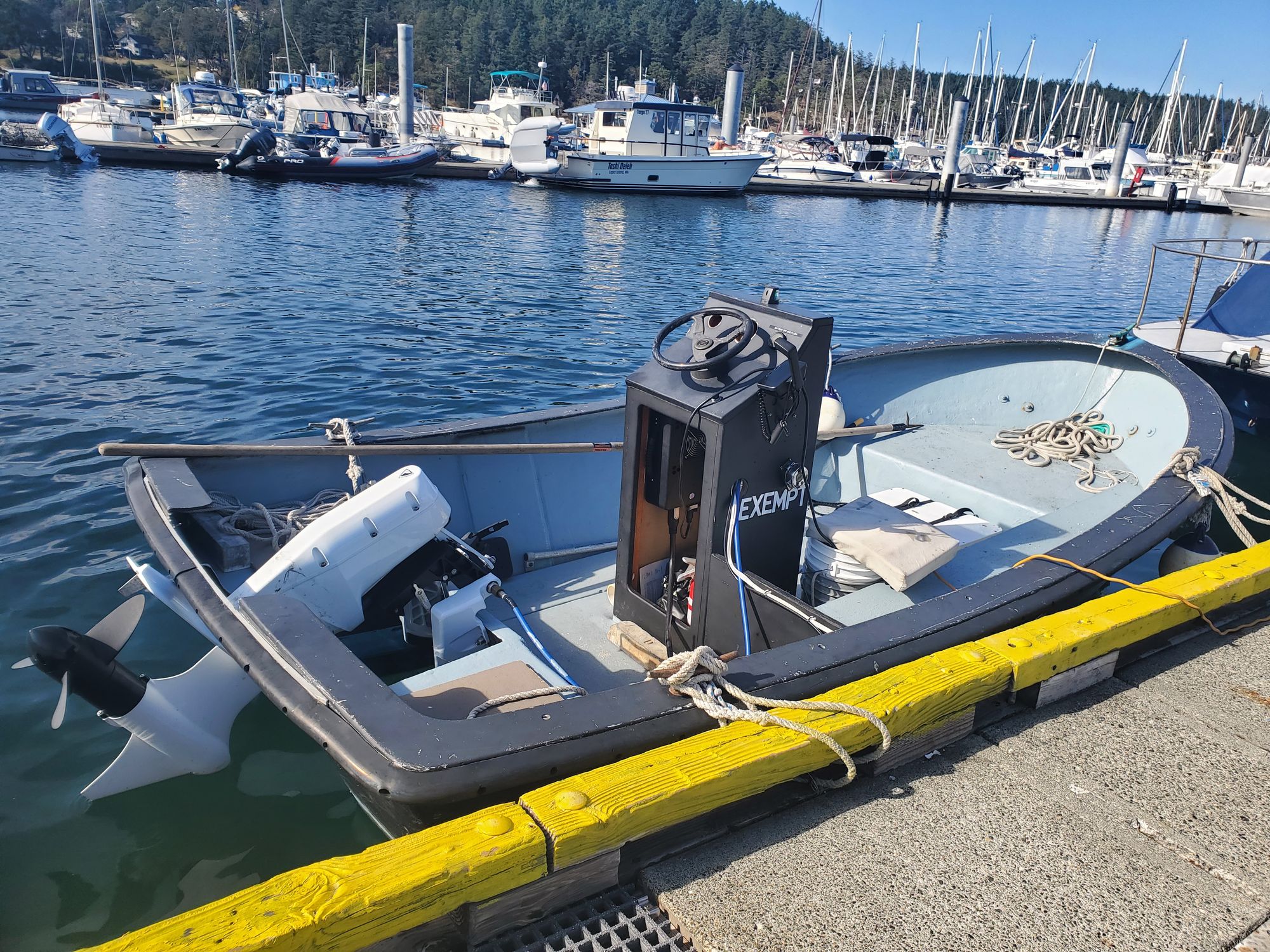 A workboat with a steering pedestal and a new, all-white outboard-style motor docked in a marina.