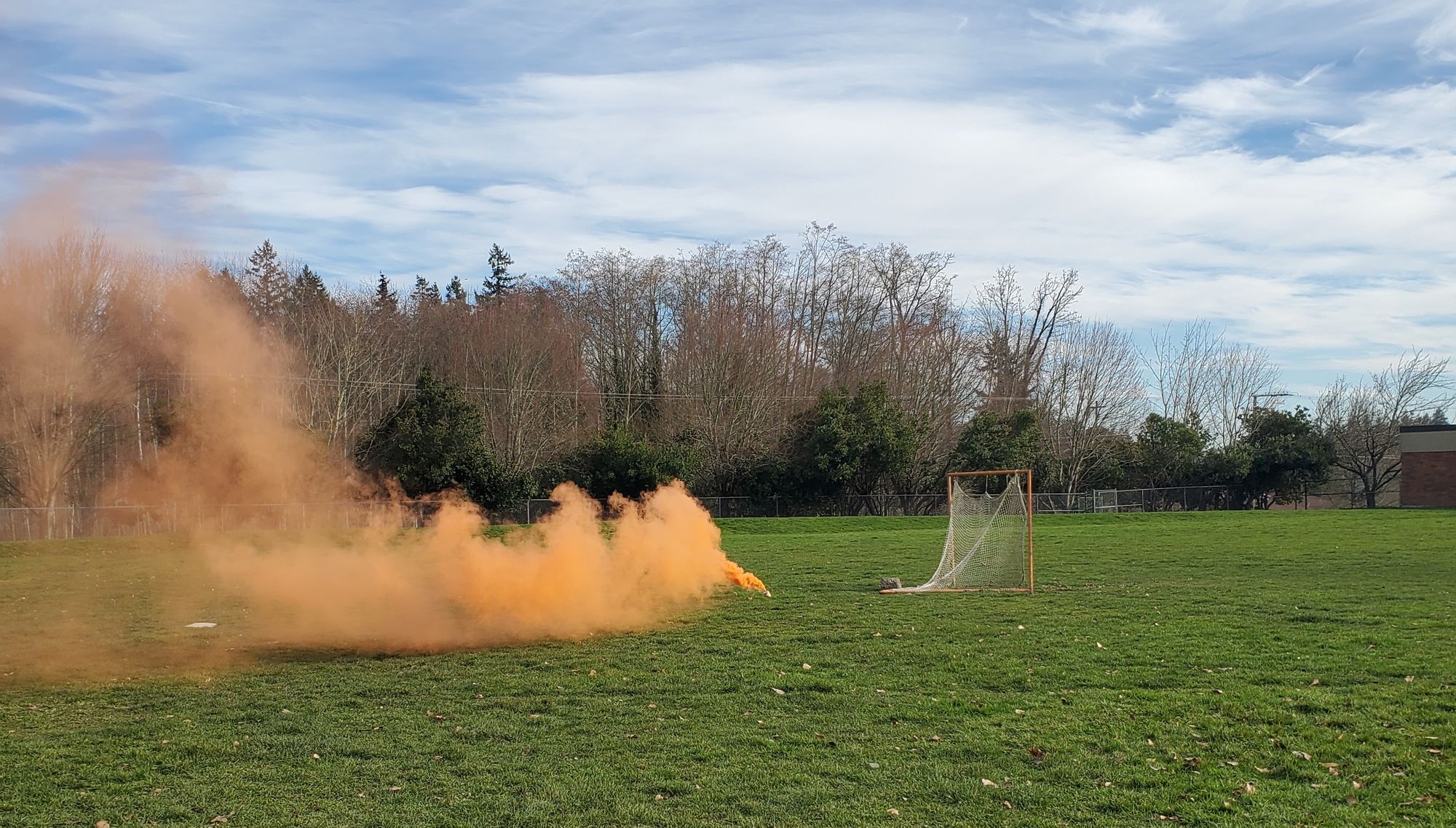 Orange smoke spreads across a field with a small netted goal nearby.