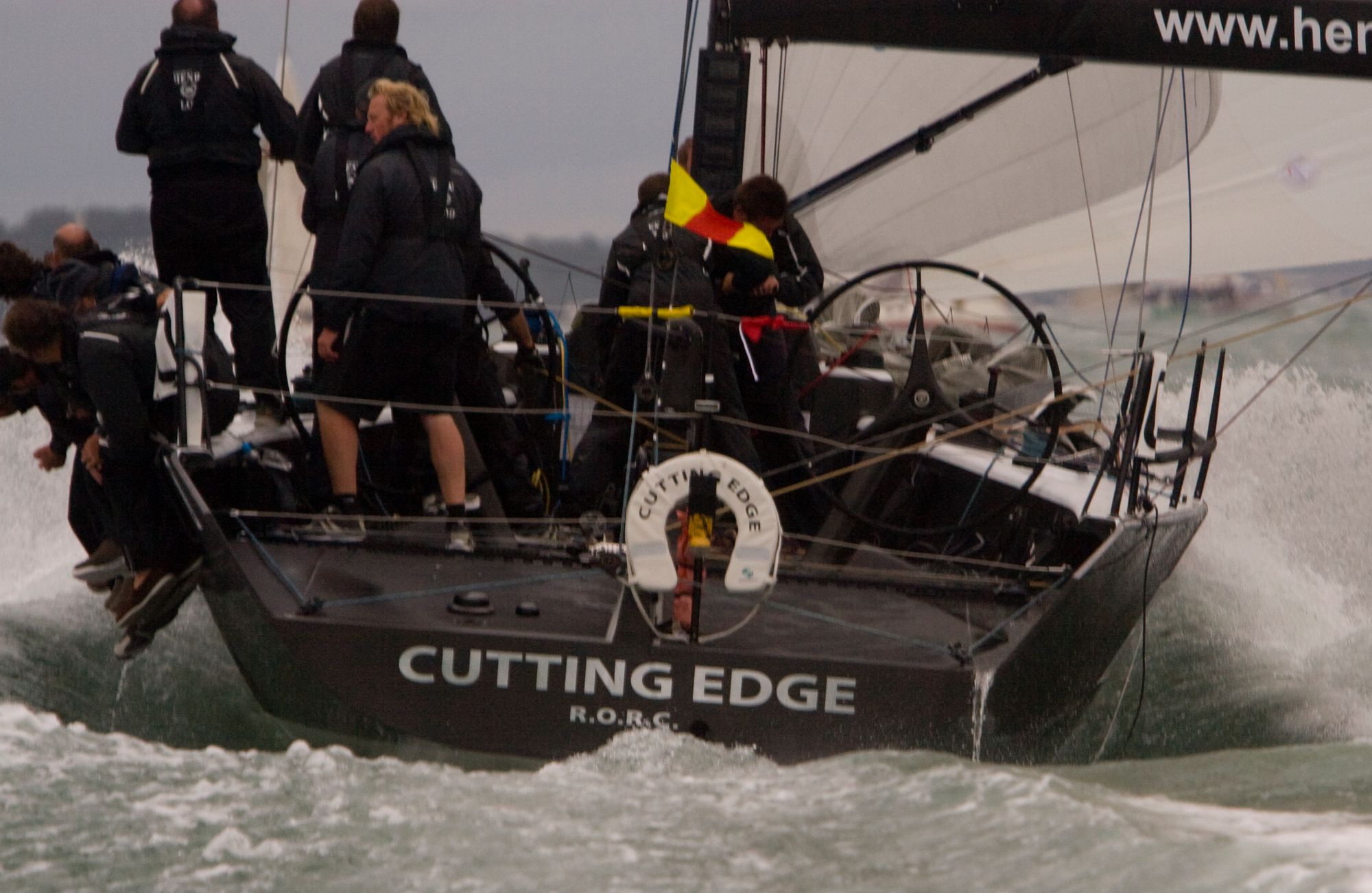 A sailboat designed for racing with over a dozen crew members sails through waves.