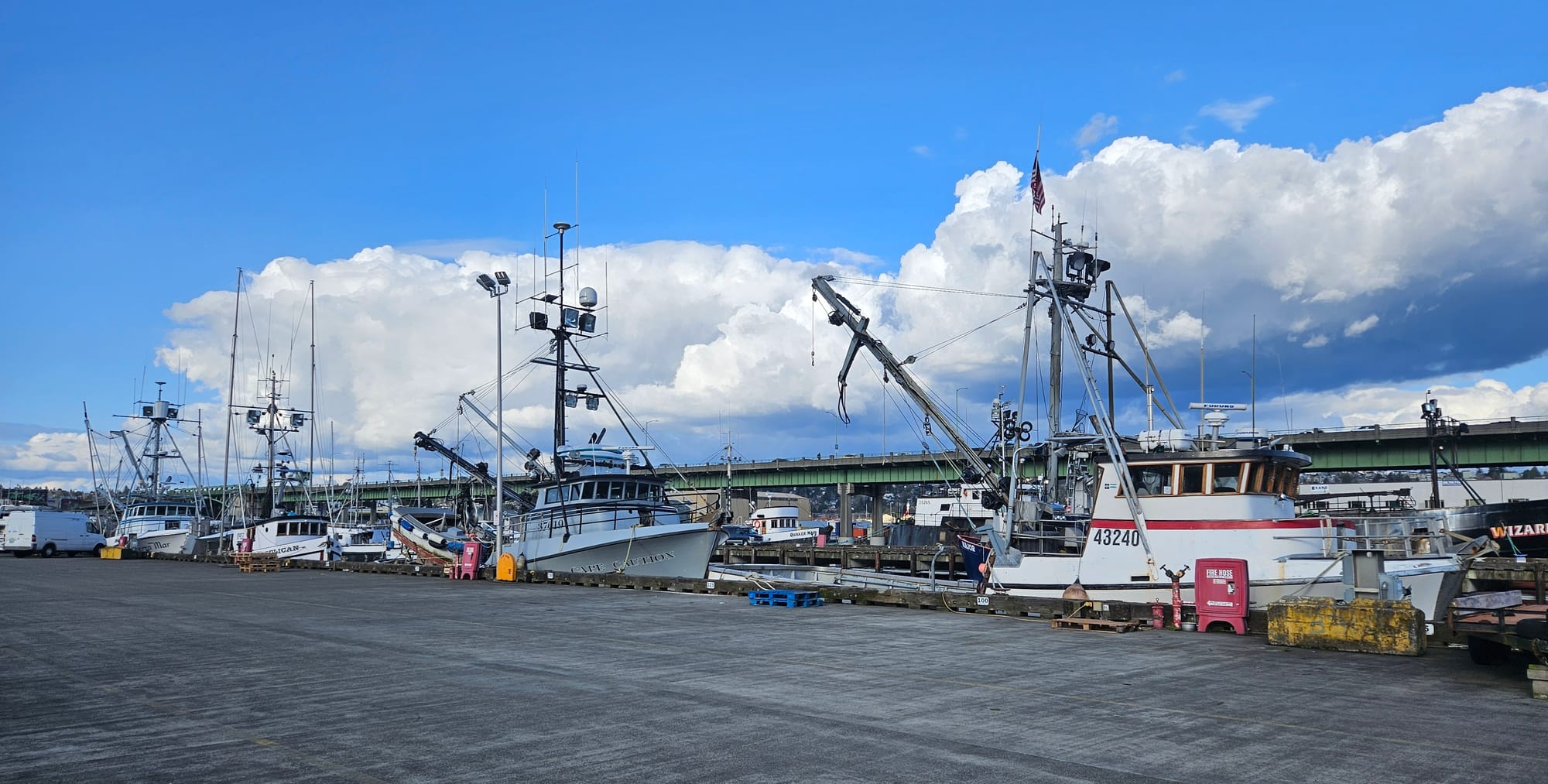 Four commercial fishing vessels tied up alongside a large dock.