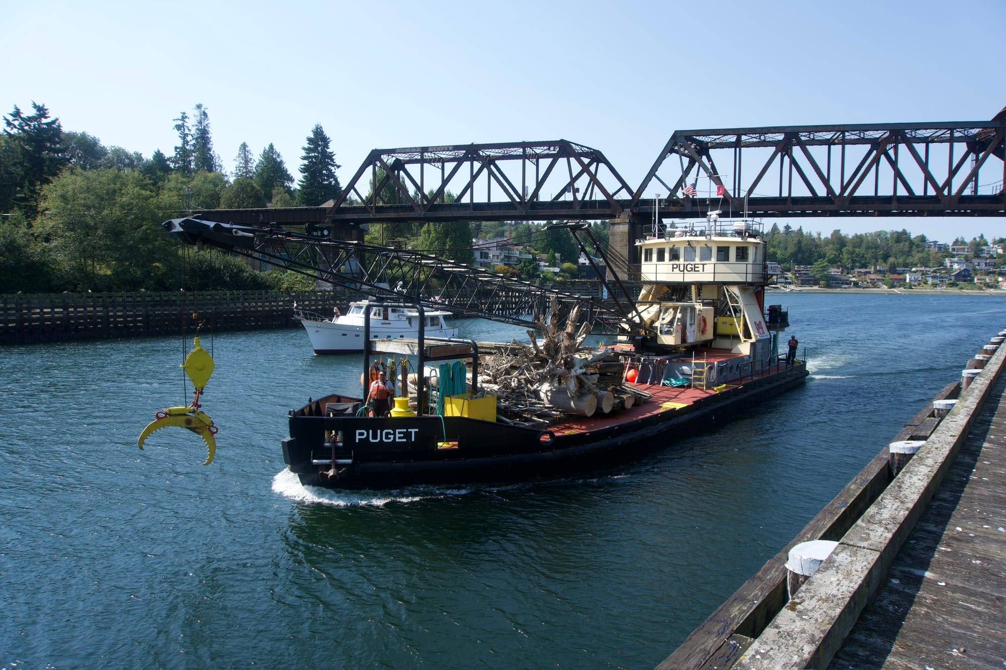 A black and white ship with a crane passes under a railroad bridge.