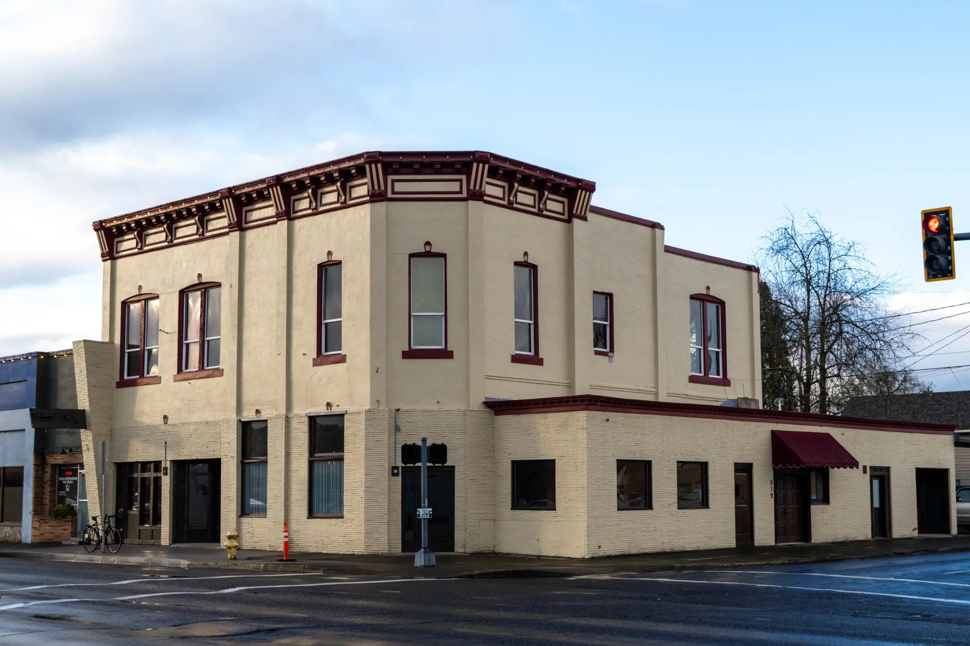 A historic looking tan building with dark red trim on a street corner.