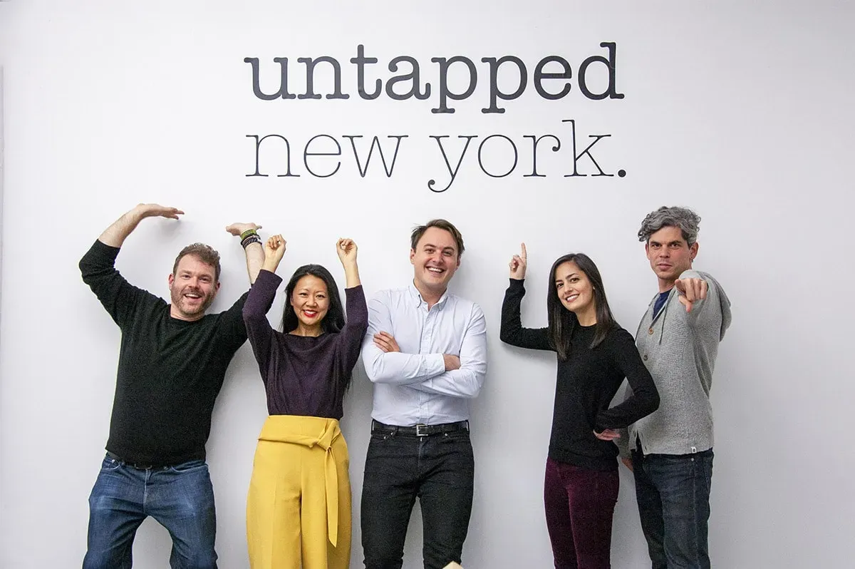 Five people smile, some with arms raised, below a sign reading "Untapped New York"