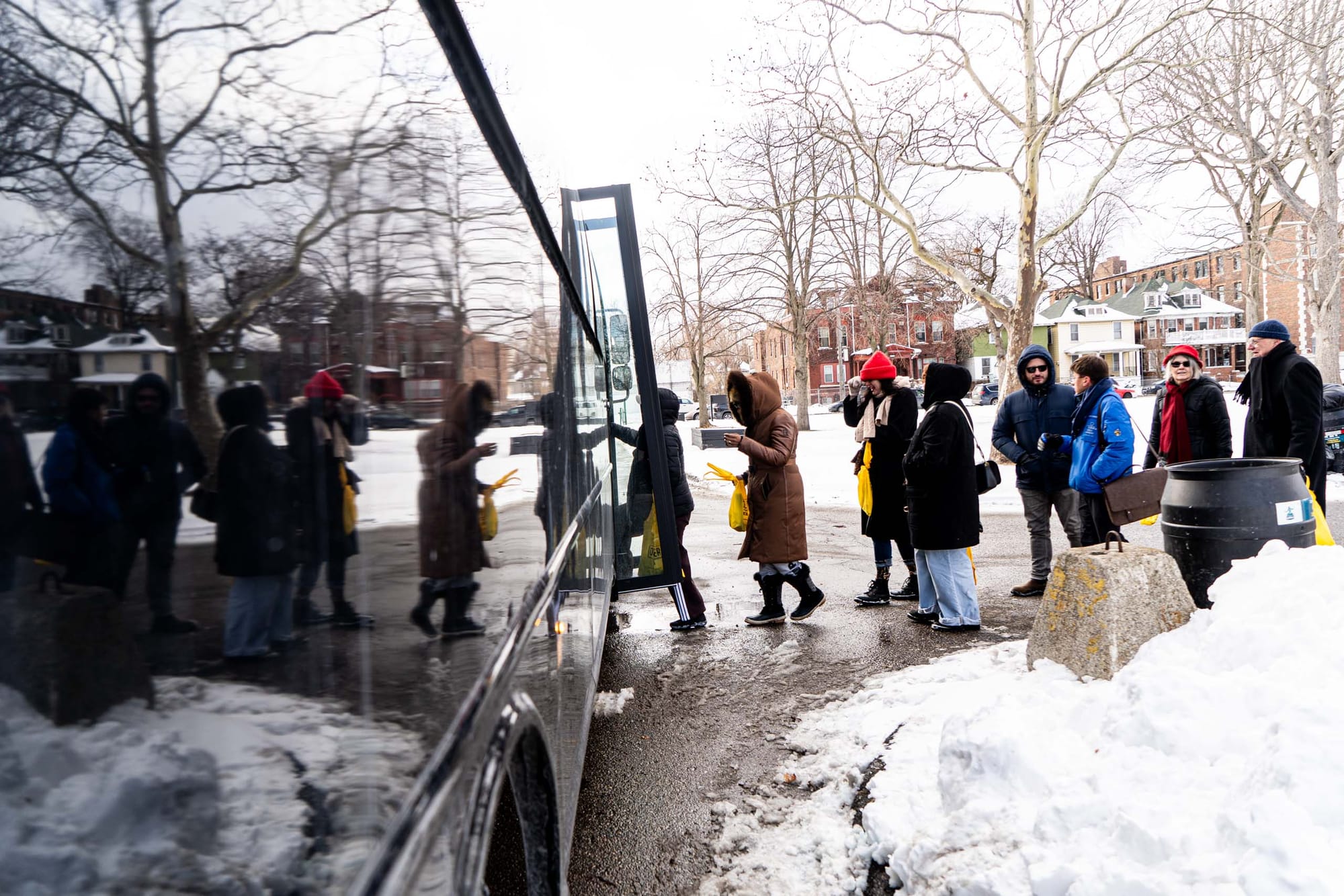 People queue to board a shiny black bus with snow on the ground.