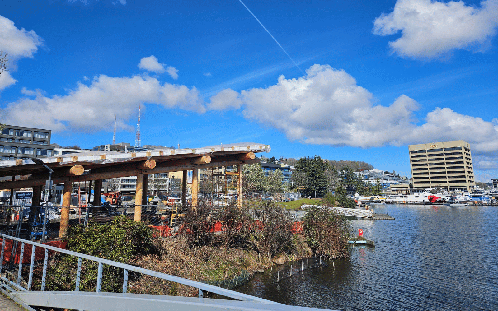 A timber building under construction next to water with city buildings and seaplanes behind.