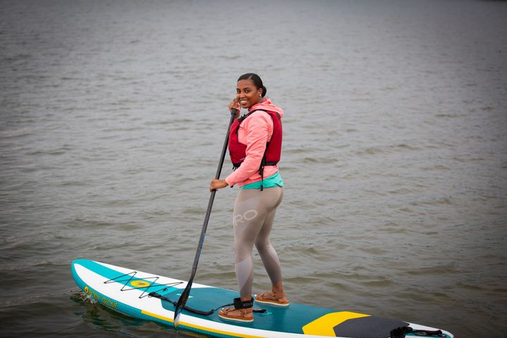 A woman smiles on a paddleboard wearing a red lifejacket.