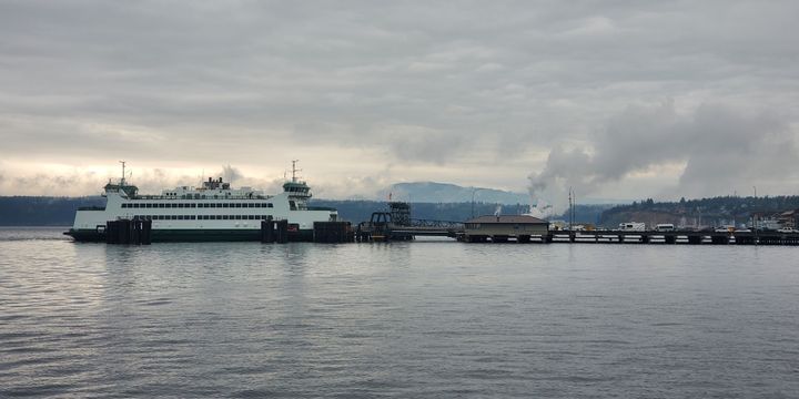 A white, double decker ferry pulled up to a dock with cars waiting.