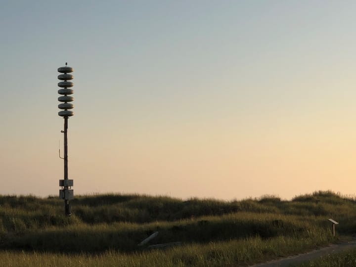 A pole with seven round devices stacked on top in a naturally grassy area.