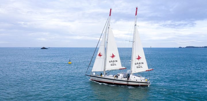 A large sailboat with three sails moves through the water pass a buoy and rocks.