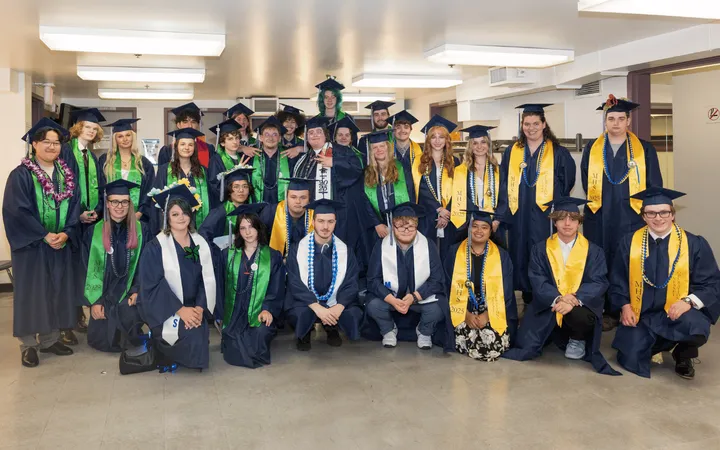Students in caps and gowns with green, white or yellow sashes post for a photo