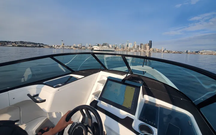 A view of a ferry and downtown Seattle beyond a boat windshield and steering wheel.