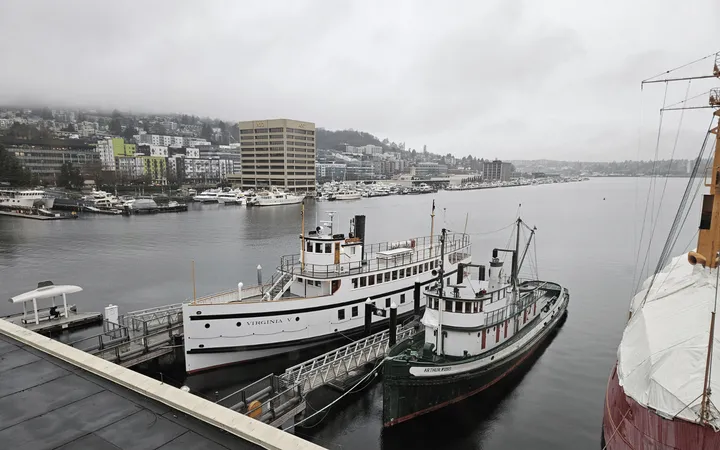 Two historic boats at a dock with a city and gray lake in the background.