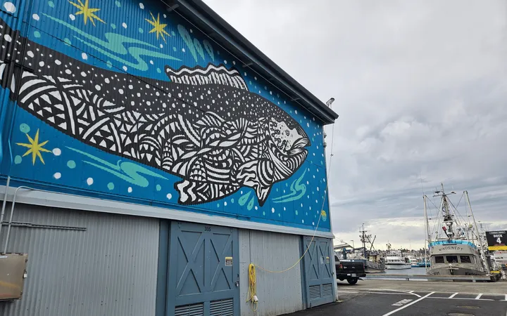 A large fish painting on a building with fishing boats in the background.